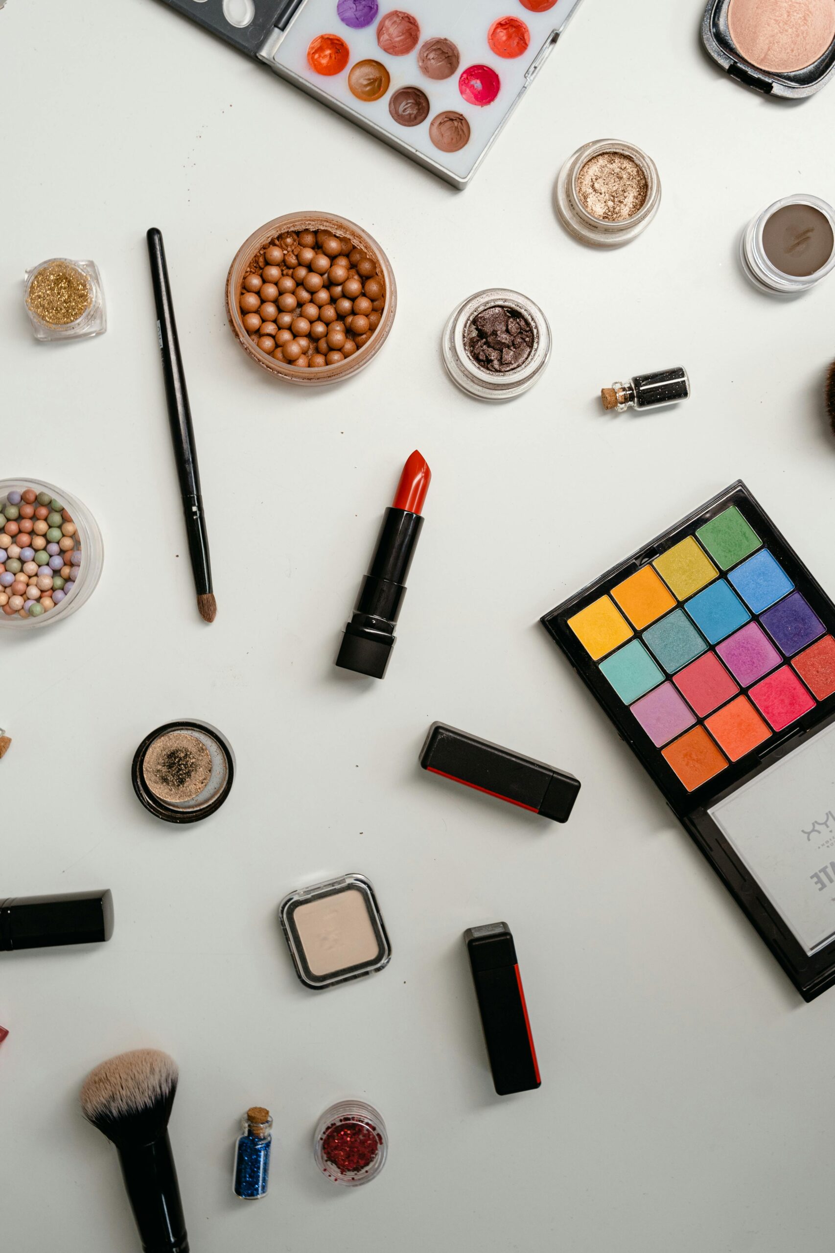 Flat lay of makeup products including brushes, lipsticks, powder, and cosmetic tools on a white background